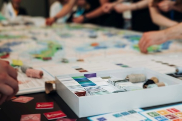 A close-up of people gathered around a table to play a board game, representing a fun and competitive game night party theme.