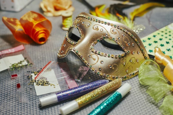 A creative DIY party theme idea showing an ornate masquerade mask surrounded by craft supplies like glitter glue, ready for decoration.