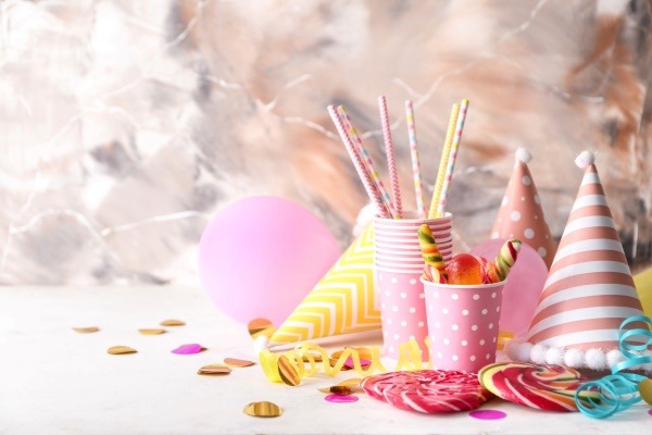 A stylish arrangement of pink and gold party supplies, including paper cups, candy, and a balloon, illustrating a party theme for adults.