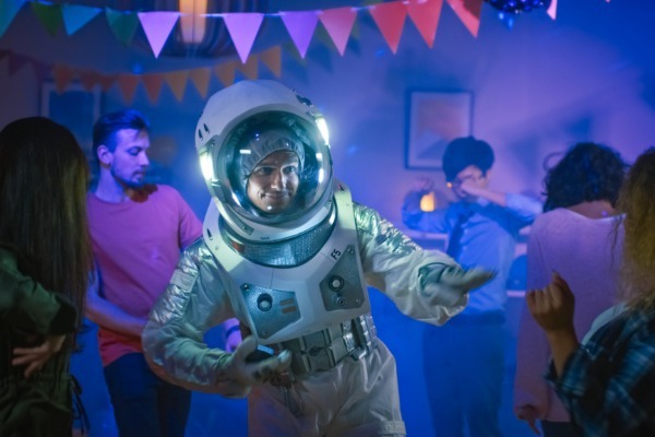 A guest dancing at a costume party dressed in a full astronaut suit with a glowing helmet, representing a creative outer space or sci-fi party theme.
