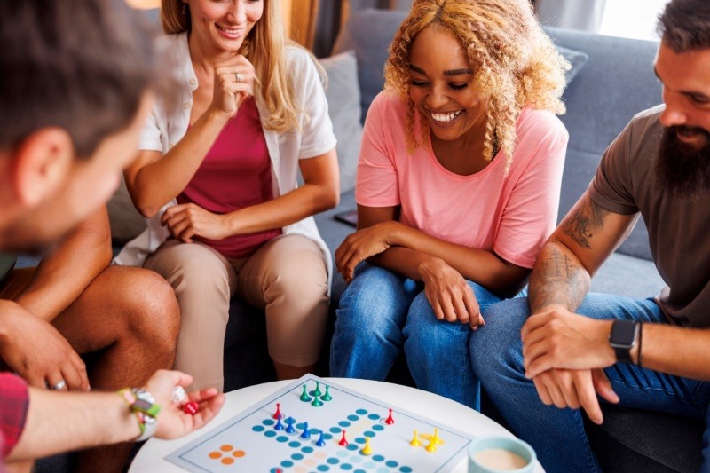 A group of smiling friends enjoying a board game night, gathered around a colorful Ludo game board for a relaxed party activity.