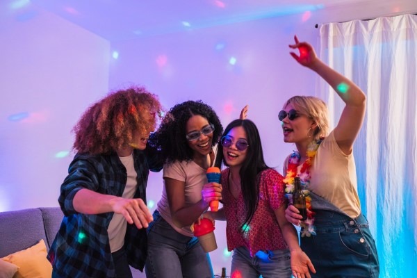 A group of friends enjoying a creative karaoke or disco party theme, dancing and singing energetically under colorful party lights.