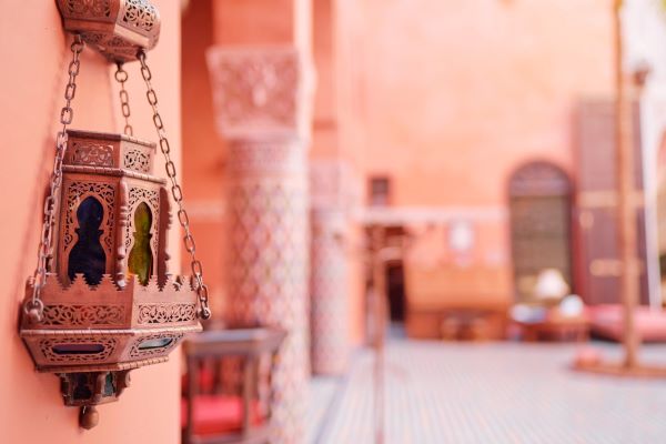 A cluster of ornate, metal Moroccan lanterns with intricate cut-out patterns hanging and glowing with warm light.