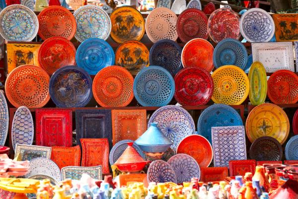 A vibrant display at a Moroccan souk showing stacks of colorful, hand-painted ceramic plates, bowls, and traditional clay cooking tajines.