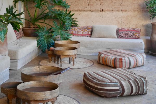 Two Moroccan leather poufs, one tan and one white, resting on a vibrant, colorful Berber-style area rug with intricate geometric patterns.