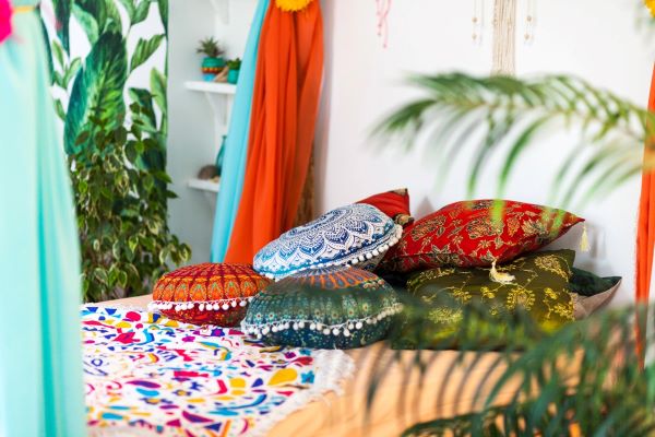 A bed in a bedroom with an assortment of decorative Moroccan throw pillows featuring tassels, stripes, and geometric patterns.