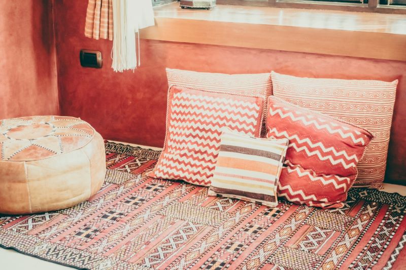 A cozy Moroccan-style living room with a low-slung sofa covered in red patterned fabric and piled high with a variety of colorful, textured throw pillows.