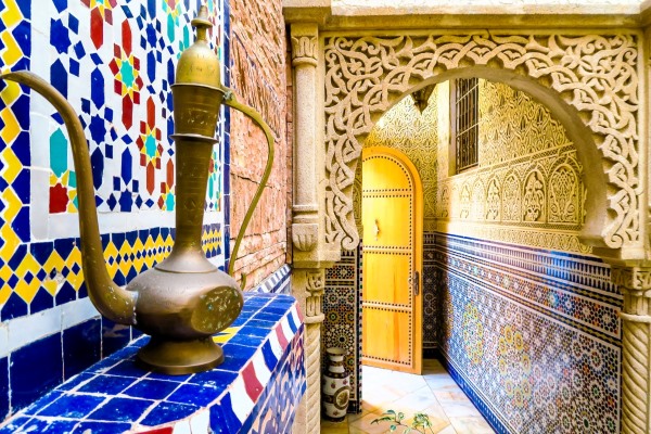 A stunning, vibrant gold and blue arched doorway in a Moroccan house, with an ornate dark metal decor standing on the left side.